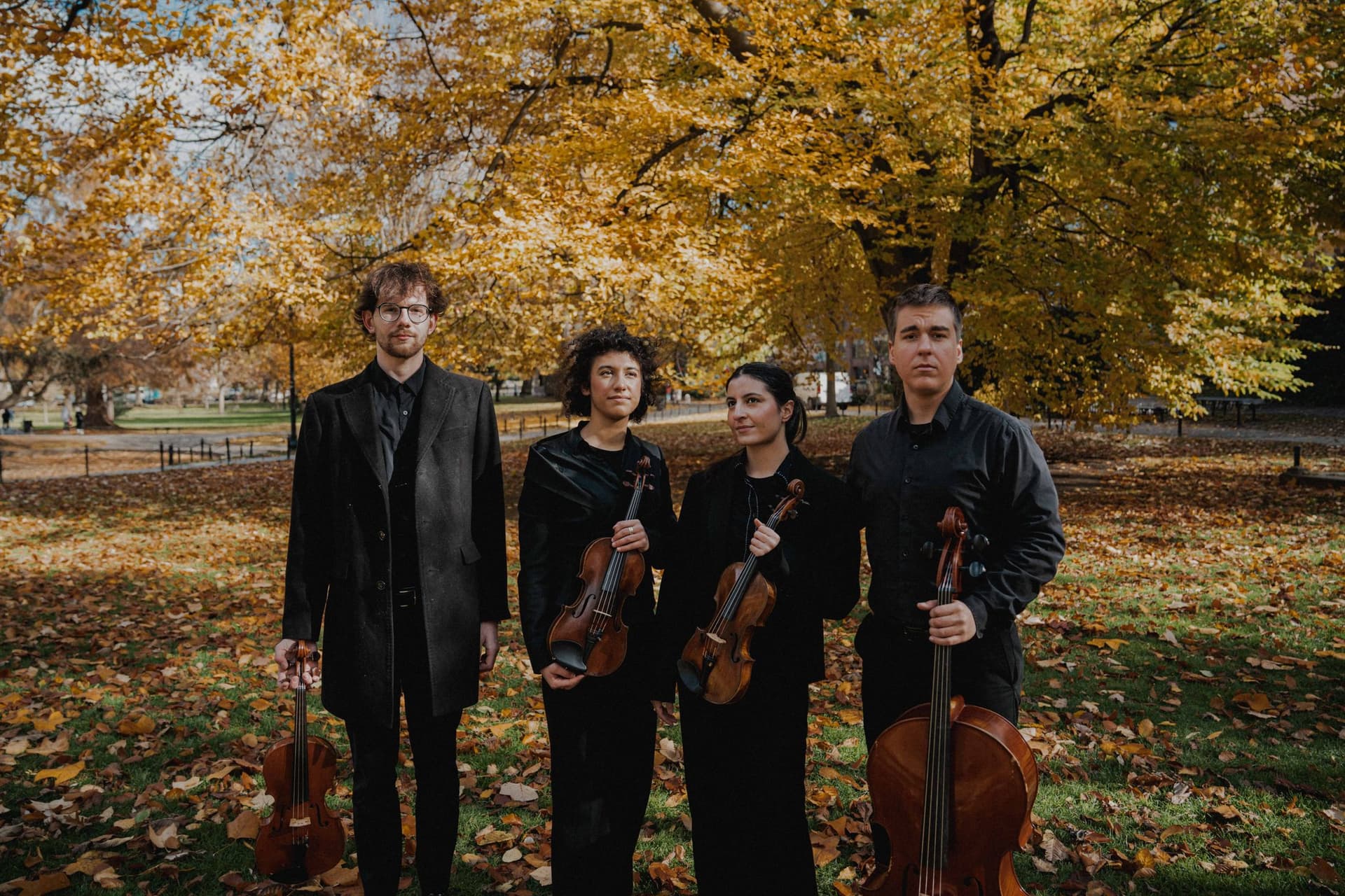 The quartet with violin, viola, and cello under autumn trees